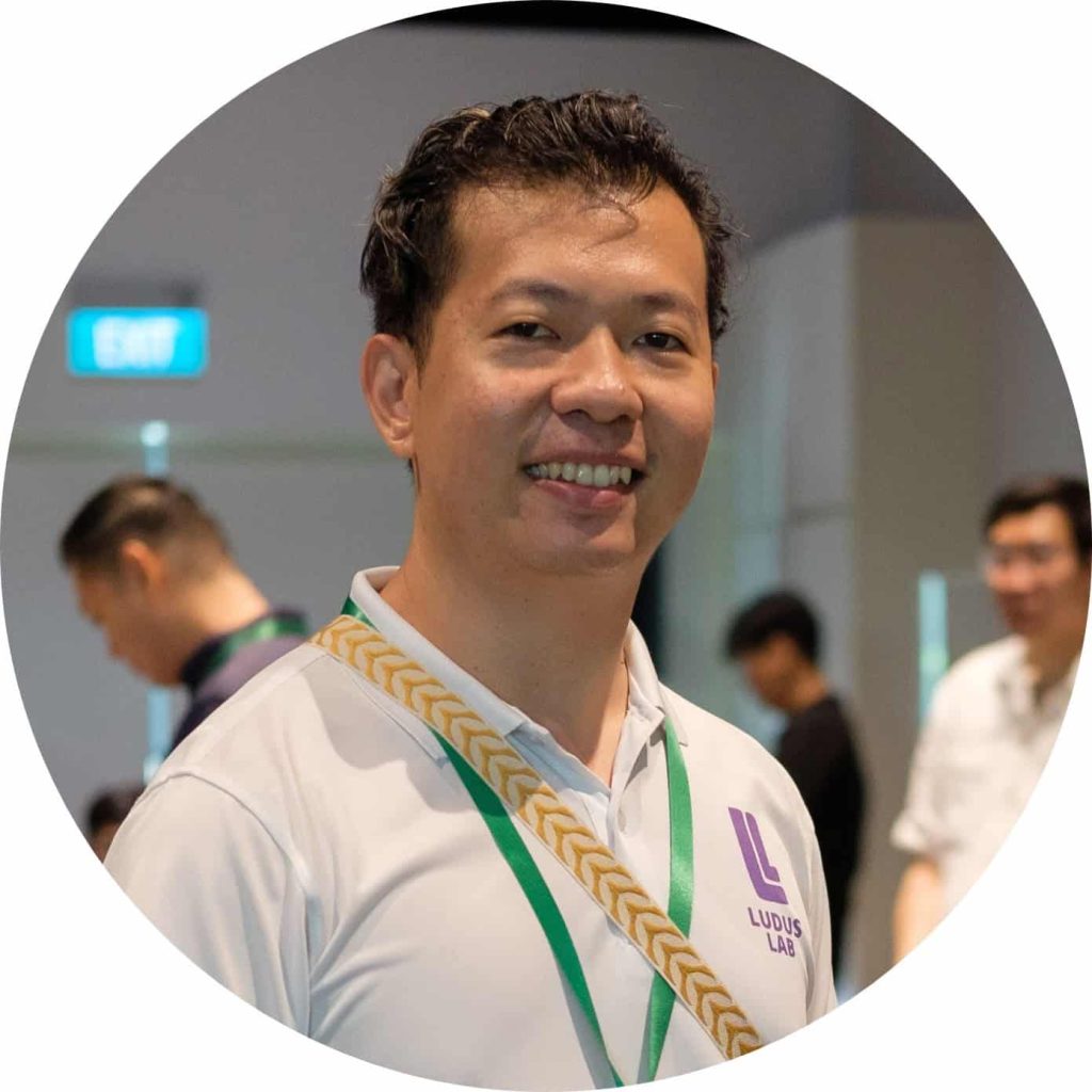 Smiling Ludus Lab guide in a white polo shirt and green lanyard at an indoor event