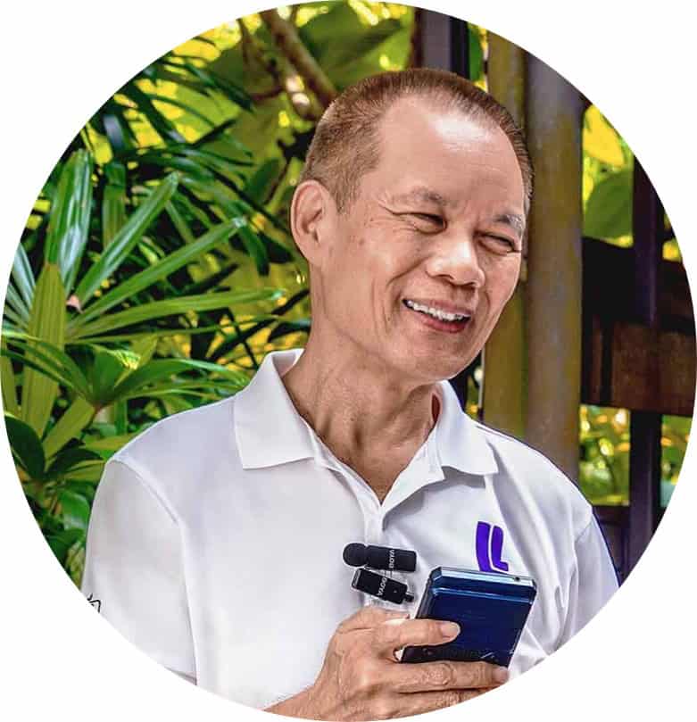 Smiling Ludus Lab guide in a white polo shirt holding a smartphone, with a clip-on microphone and greenery in the background