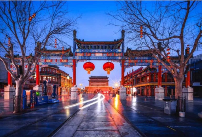 Beijing Senior Tour - Traditional Chinese paifang archway with red lanterns marking the entrance to Beijing's historic Qianmen Street at dusk.