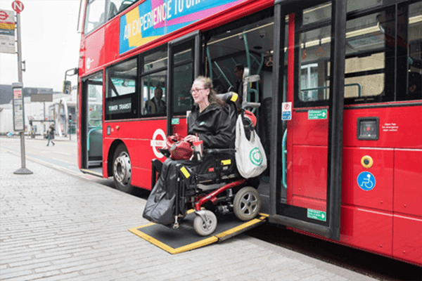 A wheelchair user exits a red public bus using an extended accessibility ramp at a bus stop. 