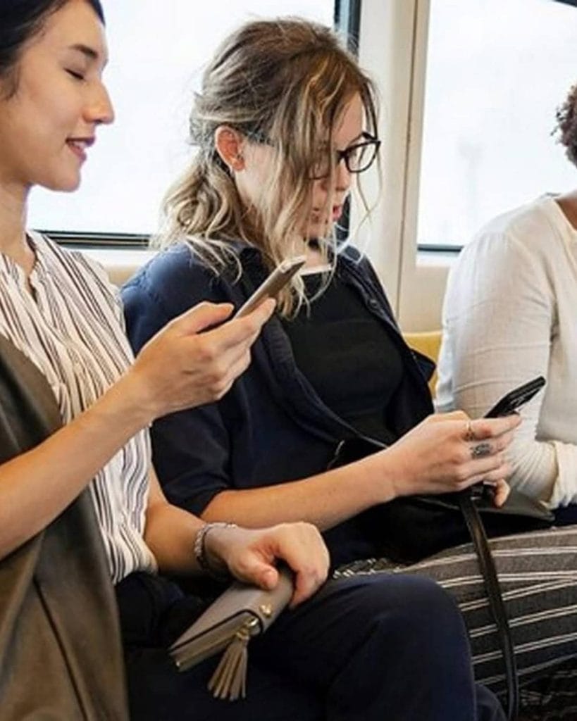 A diverse group of commuters seated inside a train while using their mobile phones.