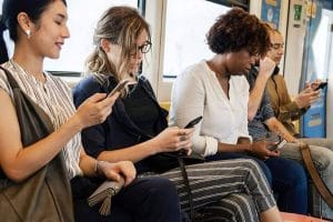 A diverse group of commuters seated inside a train while using their mobile phones.