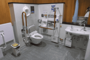 Spacious accessible public toilet in Japan with grab bars, an adult changing bench, emergency controls and a wheelchair-accessible sink.