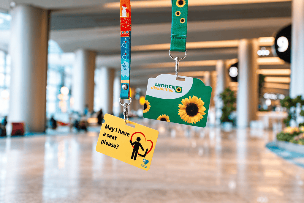 Two hidden-disability awareness lanyards displaying “Hidden Disabilities” and “May I have a seat please?” cards in a bright indoor public space.