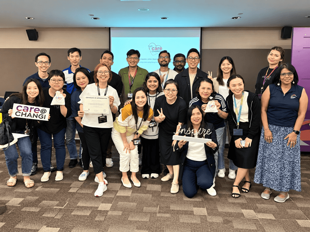 A diverse group of Care@Changi participants posing together with a certificate and appreciation gifts after an inclusive community programme.
