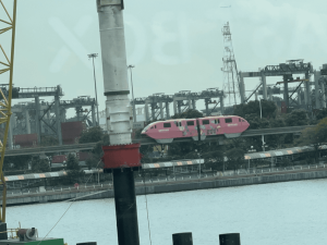 Pink Sentosa Express monorail travelling along an elevated track with Singapore’s port cranes in the background.